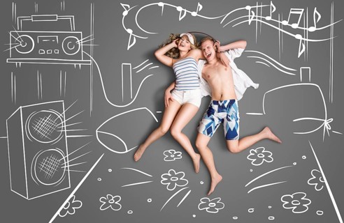 Love story of a romantic couple lying in bed, sharing headphones and listening to music against a