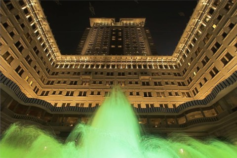 The jets of a fountain illuminated by green light before an enormous architectural complex in Hong