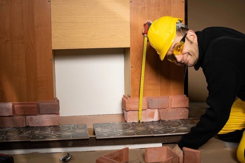 The construction worker looks at the camera and smiles while measuring. Wearing personal protective