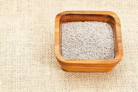 White chia seeds in square wooden bowl against burlap canvas