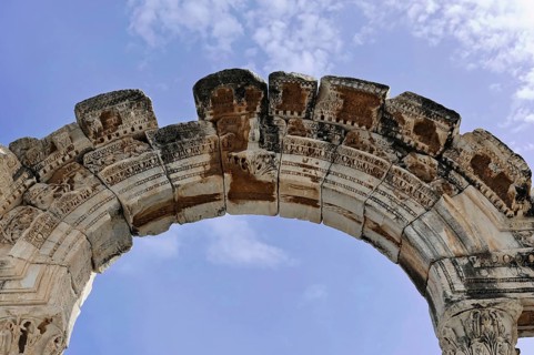 Ancient stone arch with decorative details against a blue sky, Turkey, Ephesus: Tourists encounter