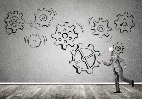 Young handsome businessman wearing white paper crown running and gear mechanism on wall