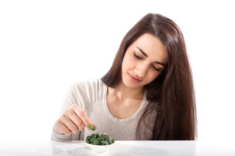 Beautiful happy healthy girl in her 20s with green dietary supplements chlorella, spirulina and