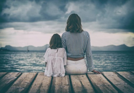 Woman and little girl sitting on the wooden pier near the sea