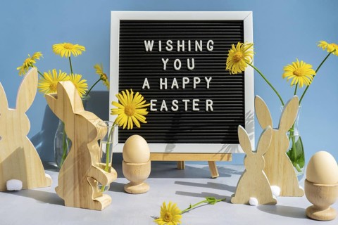 WISHING YOU A HAPPY EASTER text on letter board with bunny wooden figures and fresh flowers. Easter
