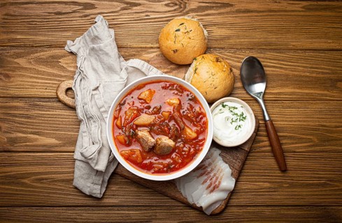 Ukrainian Borscht, red beetroot soup with meat, in white bowl with sour cream, garlic buns