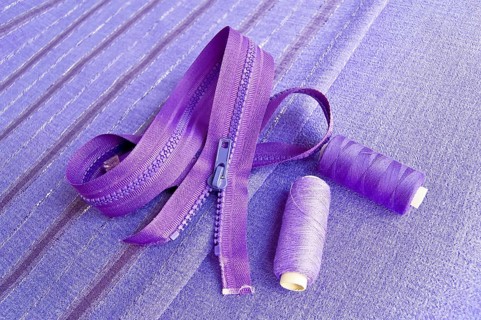 Locking zipper and two reels of thread on the purple plain and striped fabrics