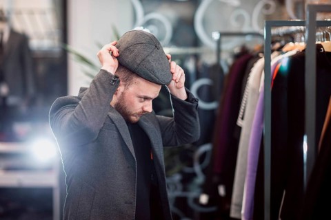 Individual trying on a flat cap in a fashionable clothing store setting