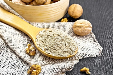 Walnut flour in a spoon on burlap, nuts on a table and in a bowl against dark wooden board