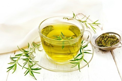 Rosemary herbal tea in a cup, a strainer with dry herb and a linen napkin on the background of a