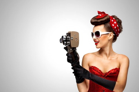 Retro photo of a pin up girl with an old 8 mm camera on a grey background