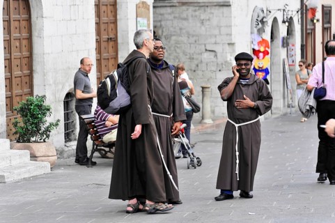 Group of monks in traditional robes on a busy city street, Assisi, Umbria, Italy