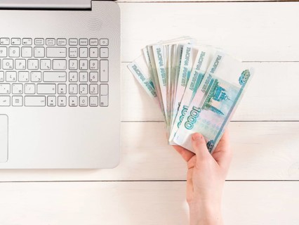 Hand holding russian rubles near laptop on white wooden background. Top view or flat lay. Finance