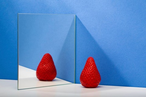 A fresh and tasty strawberry reflected in the mirror on the blue background. Fresh strawberry in