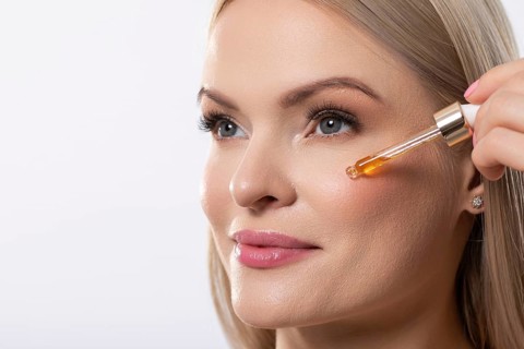 A woman gently applies a brightening serum to her face, promoting radiant and healthy skin with
