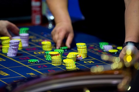Roulette table with human hands putting down chips in casino. Roulette wheel in the foreground.