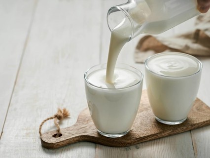 Pouring homemade kefir, buttermilk or yogurt with probiotics. Yogurt flowing from glass bottle on