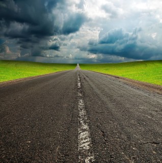 Old broken asphault road in green field over blue cloudy sky