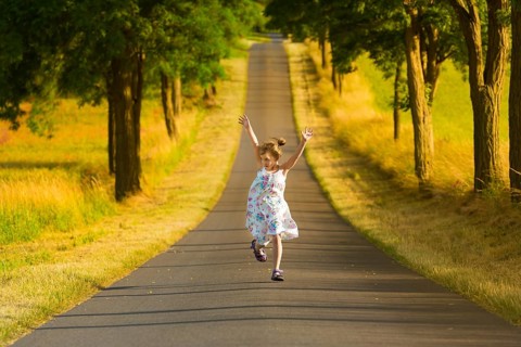 A little girl in a summer dress runs along a street in the light of a summer evening, jumping and