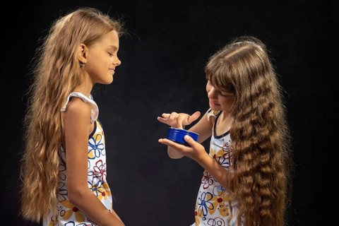A girl puts jar cream on her finger, another girl sits nearby