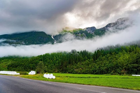 Wide asphalt road crosses the valley. Jostedalsbreen Park. Valley surrounded by high forested