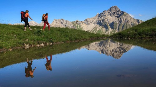Two female mountaineers are reflected in a lake by the majestic Biberkopf in the background, Allgäu