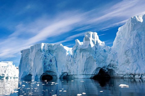 Ice formations with caves and reflections in the water under a blue sky, icebergs in the Southern