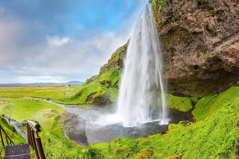 Seljalandsfoss waterfall in July. Large rainbow decorates a drop of water. The warm July day in