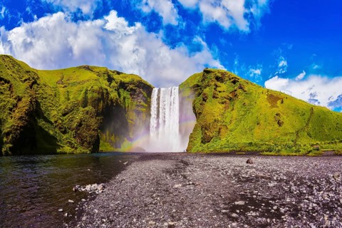 Iceland, waterfall Skogafoss summer, clouds of mist. Huge picturesque waterfall flowing from under
