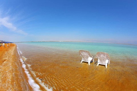Two white beach armchairs stood side by side in the water at the beach. Dead Sea, Israel