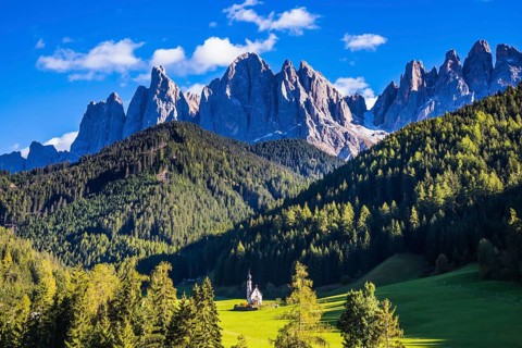 Dolomites, Tirol. Sunny autumn day. Rocky peaks and forested mountains surrounded by green Alpine