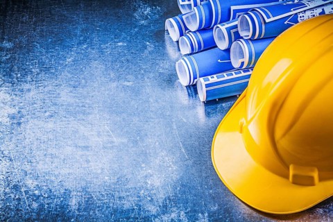 Blue engineering drawings yellow hard hat on scratched metallic background construction concept
