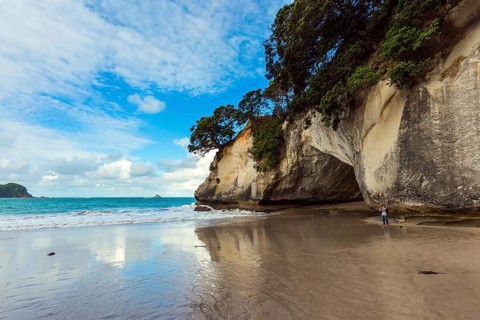 Woman takes pictures of magnificent landscape. Ocean tide in the Cathedral Cove. Mirror reflections