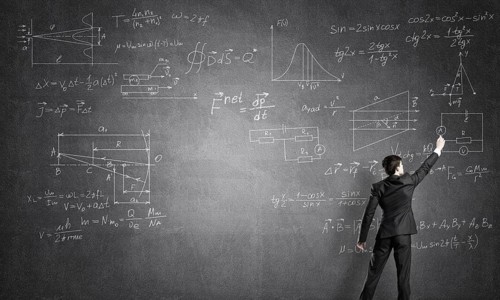 Man in suit standing with back and drawing formulas on chalkboard