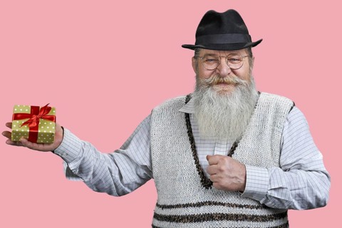 Portrait of aged man with gift box. Isolated on pink