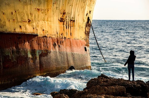 Person looking at moored shipwreck on a rocky coast line and wind waves. Paphos Cyprus