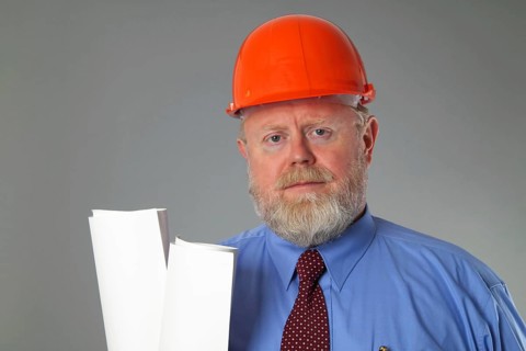 Man in suit with construction helmet on grey background