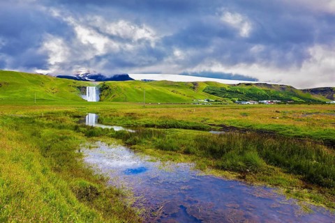 Huge full-flowing waterfall Skogafoss reflected in small creek. Spectacular reflection
