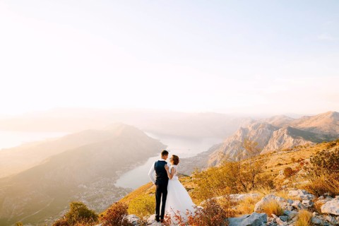 The bride and groom stand on the top of Mount Lovcen overlooking the Bay of Kotor, smile and hug
