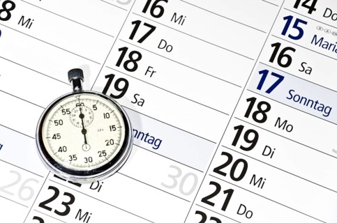 Stopwatch lying on calendar (with captions of the days of the week in German)