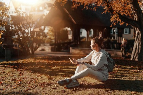 Young fashionable teenage girl with smartphone in park in autumn sitting at smiling. Trendy young