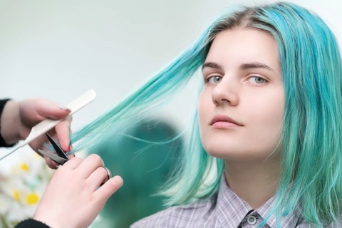 Hairdresser cutting with scissors long green hair of young woman. Hair care in professional beauty