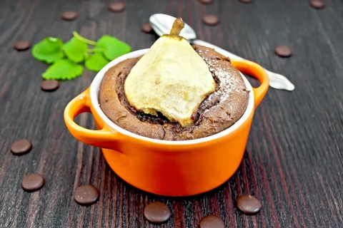 Cake with chocolate and pear in red roaster, mint and spoon on a background of dark wood planks