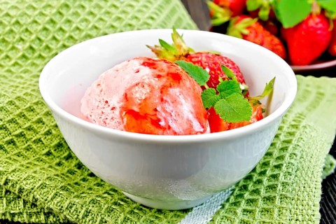 Ice cream strawberry in a white bowl with berries and syrup on a green napkin on a background of a