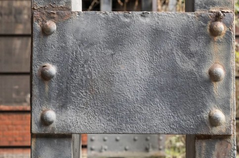 Close-up of a weathered gray metal plate attached to a larger metal structure with rivets, showing