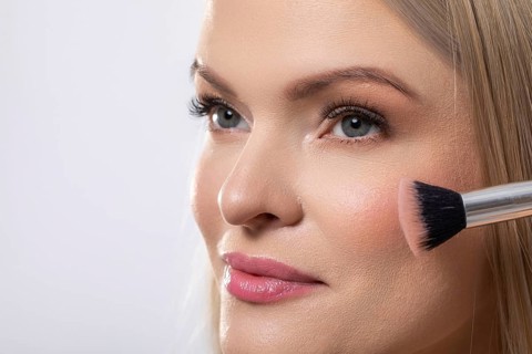This is a professional makeup application showcasing a model skillfully utilizing a blush brush for