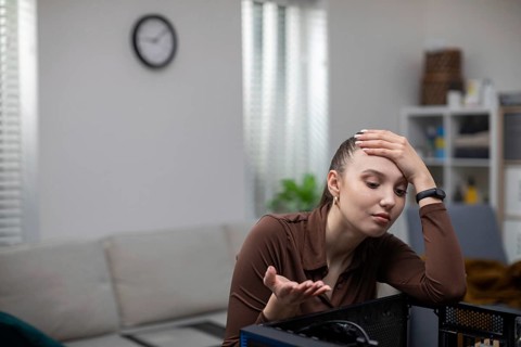 A young woman catches her head in a gesture of helplessness while fixing her computer. A girl sits