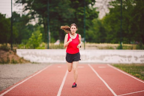 Beautiful young athlete Caucasian woman with big breasts in red T-shirt and short shorts running