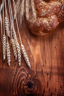 Loaf of breead and wheat ears on vintage wooden board with small copyspace food and drink concept