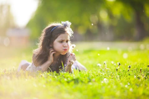 The little girl lays on a grass and blowing dandelion on the summer day